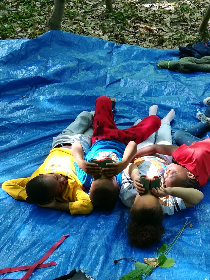 des enfants allongés observent le ciel et les arbres avec des jumelles